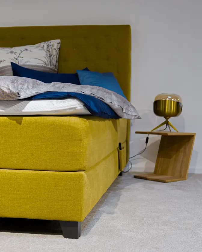 Boxspringbett mit gelbem Kopfteil und aufgeschlagener Bettwäsche